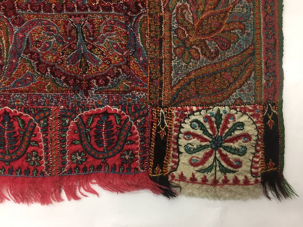 赤いショールの裾の角の部分写真。小さなペイズリーや花の刺繍と色とりどりの糸が見える